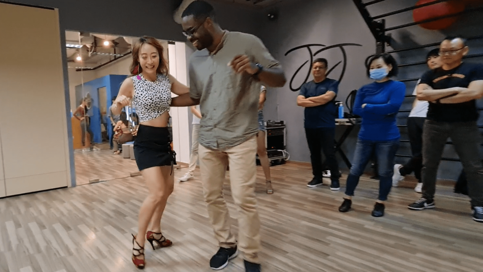 An Image of a Man and a Woman Dancing Kizomba in a Dance Studio with Students Watching While Standing